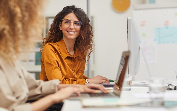 Smiling woman working on laptop with colleague