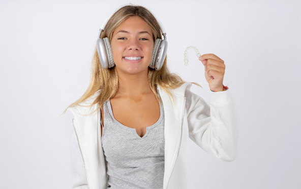 Smiling teen girl holding a clear aligner
